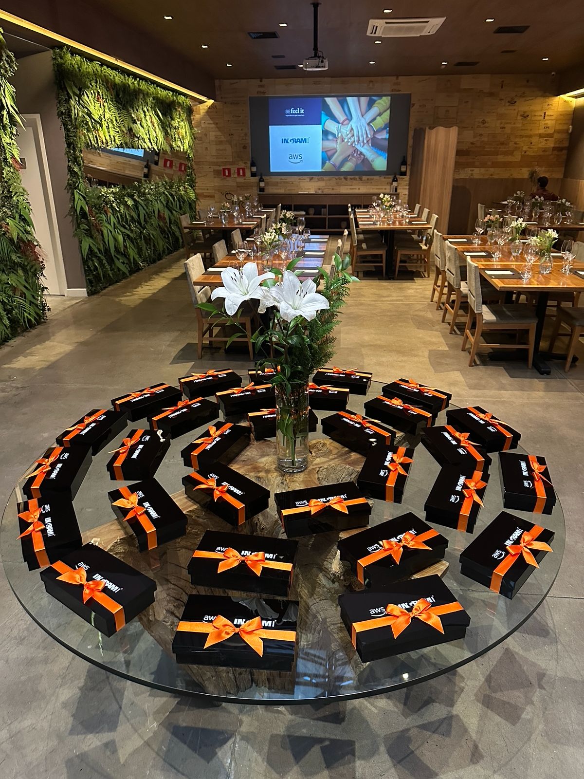 Mesa com caixas pretas organizadas em círculo e telão com logos em uma experiência personalizada da Feel It